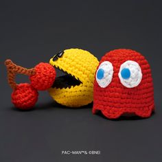 two crocheted toys sitting next to each other on a black surface, one is yellow and the other is red