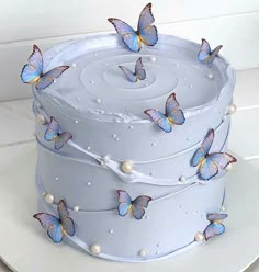 there is a white cake with blue butterflies on the top and pearls in the bottom