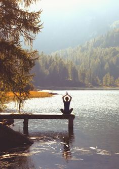 a person sitting on a bench in front of a body of water with their arms up