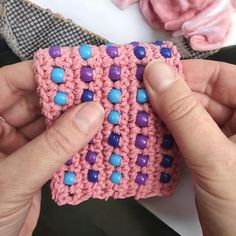 two hands are holding a pink crocheted cell phone case with blue and purple beads