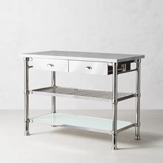 a metal and glass table with drawers on one shelf, in front of a white wall