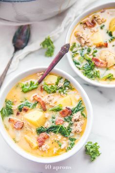 two bowls of soup with meat, potatoes and kale in them on a marble surface