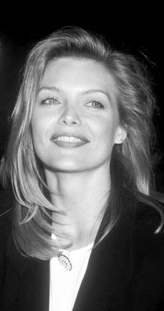 black and white photograph of a woman in a suit smiling at the camera with her hand on her hip