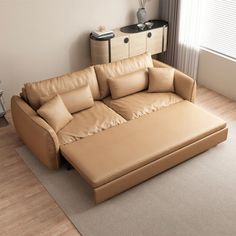 a tan leather couch sitting on top of a hard wood floor next to a window