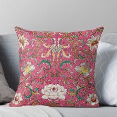 a pink pillow with white flowers on it sitting on a couch in front of a gray wall