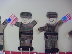 paper cut out soldiers holding american flags in front of a bulletin board with writing on it