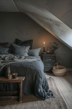 an attic bedroom with grey walls and bedding, wooden flooring, two night stands and a small side table