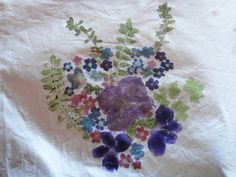 a white t - shirt with purple flowers and green leaves painted on the front side