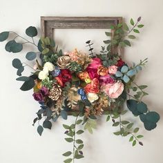 an arrangement of flowers and greenery in front of a wooden frame on the wall