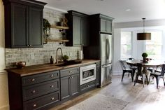 a kitchen with dark gray cabinets and white brick backsplash, wood flooring