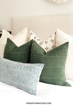 two green pillows sitting on top of a white bed next to a wall mounted clock