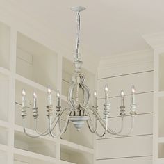 a chandelier hanging from the ceiling in a room with white walls and cabinets