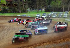 a group of dirt racing cars driving around a track with trees in the back ground