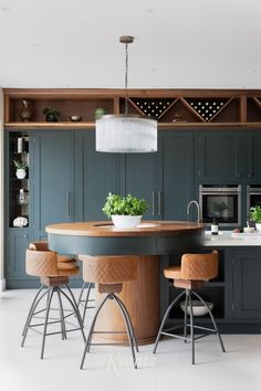 a kitchen with dark green cabinets and wooden stools, white flooring and an island in the middle