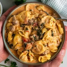 two hands holding a bowl of pasta with meat and spinach