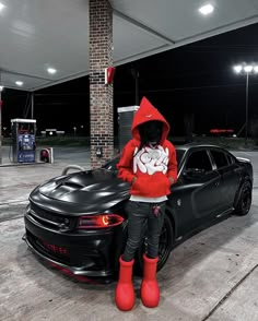 a person in a red hoodie standing next to a black car at a gas station