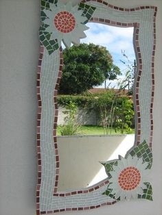 a mosaic mirror with flowers on it in front of a white wall and green grass