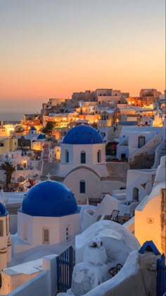 the sun is setting over some white buildings with blue domes in front of an ocean