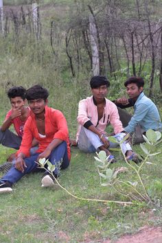 four young men sitting on the ground with trees in the background