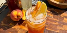 an iced drink with orange peels and lemon wedges on the rim next to some peaches