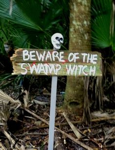 a sign that says beware of the swamp witch in front of some plants and trees