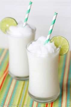 two glasses filled with milk and limes on top of a table