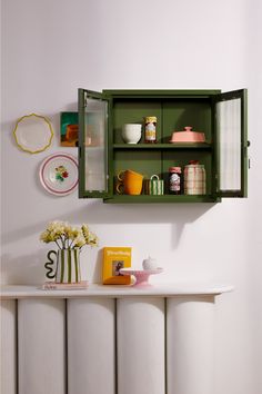 a green cabinet with dishes and cups on the shelf above it is next to a white radiator