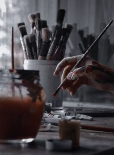 a person is painting on a table with paintbrushes and other art supplies in the background