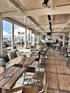 an empty restaurant with wooden tables and chairs on the floor, looking out onto the water