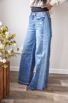 a woman standing in front of a plant wearing high waist jeans and a white sweater