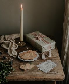 a wooden table topped with cookies and a lit candle next to a gift box on top of it