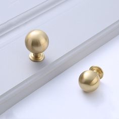 two gold knobs on the side of a white cabinet door, one with a ball