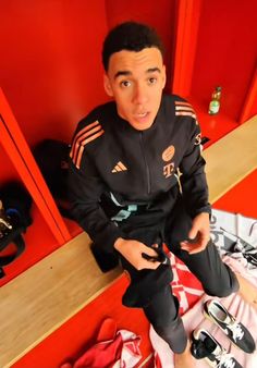 a young man sitting on top of a red bench next to some shoes and other items