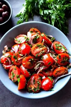 a blue bowl filled with tomatoes and onions next to olives, parsley and cilantro