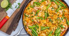 a skillet filled with noodles, shrimp and green beans on top of a cutting board