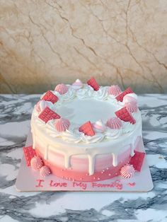 a white cake with pink icing and seashells on the top sitting on a marble table