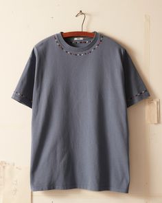 a blue t - shirt hanging on a wooden hanger next to a white wall