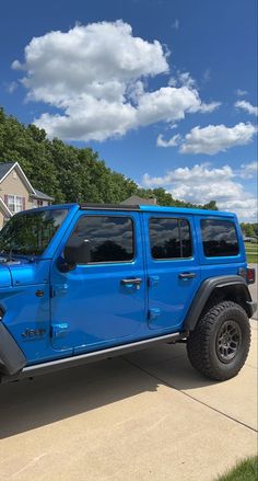 a bright blue jeep parked in front of a house on a sunny day with white clouds