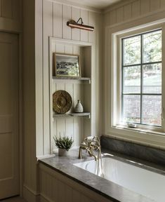 a bathroom with a tub, sink and shelves on the wall next to it's windows