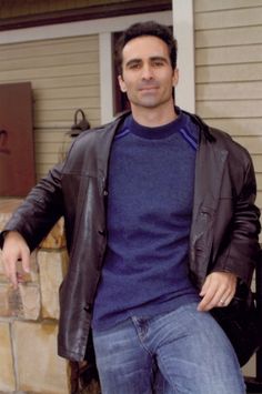 a man is sitting on a bench in front of a house and posing for the camera