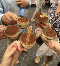 four people are holding small sandwiches with chocolate frosting on them and straws in their hands