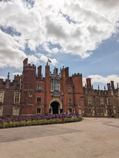 an old brick building with purple flowers in the foreground and clouds in the background