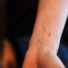 a small cross tattoo on the wrist is shown in close up view, it looks like someone has been inked