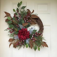 a wreath with red flowers and greenery hanging on a door