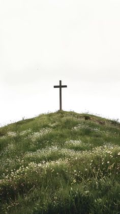 a cross sitting on top of a hill covered in grass