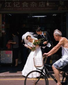 a man riding a bike next to a woman in a wedding dress on the street