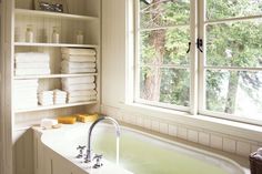 a bath tub sitting next to a window filled with white towels and other bathroom items