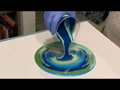 a person in blue gloves is pouring liquid into a glass bowl on top of a table