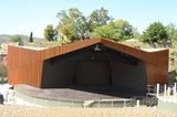 an empty stage in the middle of a field with trees and hills behind it,