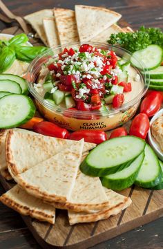 a wooden cutting board topped with sliced cucumbers, tomatoes and pita bread